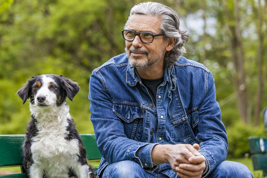 Portrait of man with grey hair and beard sitting beside his dog on a bench