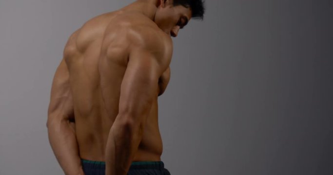A body builder filmed from behind. He is displaying his strong back muscles by flexing.