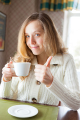 Young woman with a cup of coffee in hand showing thumb up sign