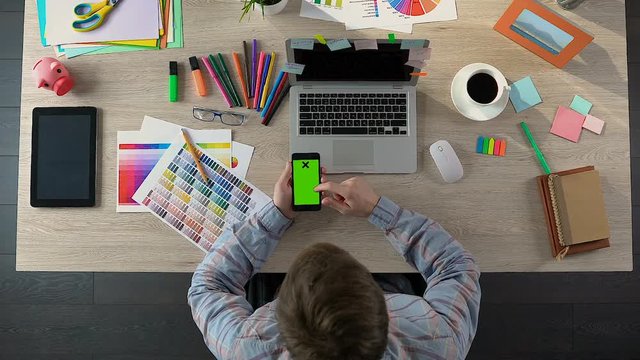 Male decorator scrolling on smartphone with green screen, freelance application