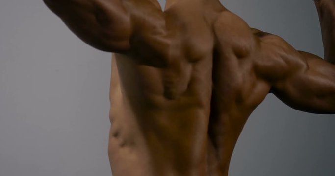A body builder filmed from behind. He is displaying his strong back muscles by flexing.