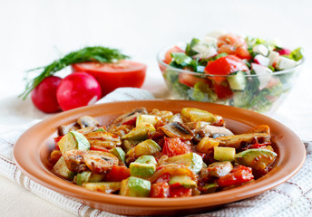 Roasted vegetables on a rustic plate. Salad with fresh vegetables in the background