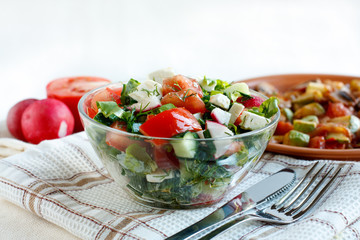 Salad with fresh vegetables and feta cheese. Roasted vegetables in the background