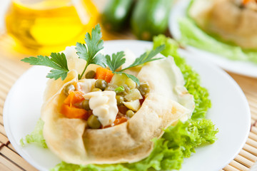 Salad with cooked vegetables and greens wrapped in a pancakes on a plate