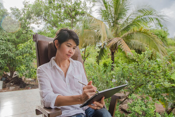 Women using tablet computer on wooden chairs  in the garden .