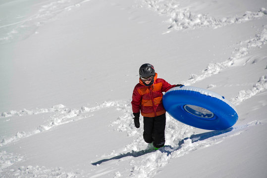 Teenage boy carrying blue blowup inflatable sledding tube up snowy hill