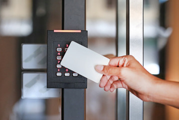 Door access control - young woman holding a key card to lock and unlock door. - obrazy, fototapety, plakaty
