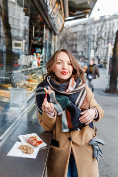 Street portrait of smiling beautiful young woman buying fast food snacks at stall in europe