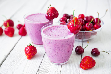 Cherry, blueberry and strawberry smoothie and tasty berries on white wooden table. Fresh natural milkshake