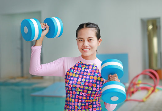 Fit smiling woman holding foam water dumbbells at swimming pool.