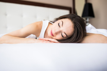 Obraz premium Woman lying at the end of the bed underneath the quilt and smiling, with her head resting upon her hand with the other in her hair.