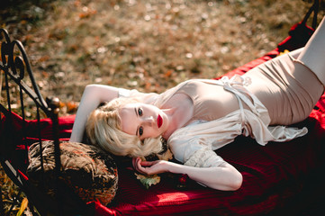 Beautiful and elegant blonde woman with red lips and hair waves wearing beige nightie posing on the...