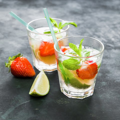 Two glasses of strawberry mojito on dark background.
