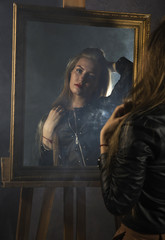 beautiful young woman in a leather jacket looks in the mirror as her portrait