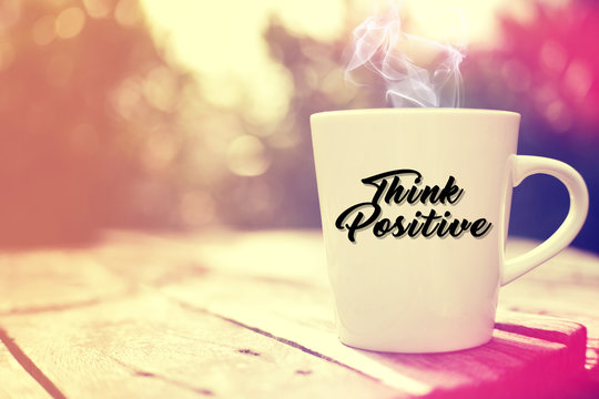 White cup on wooden background. Written "Think Positive".