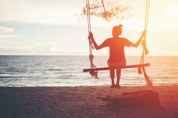 Young woman sitting on a swing at the beach.