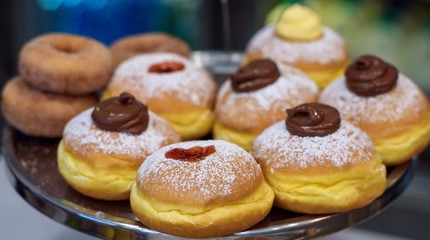 Many jam and chocolate donuts on a serving plate presentes in a shallow depth of field.