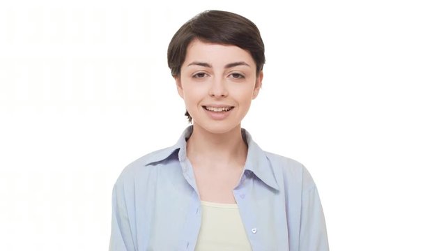 Young brunette Caucasian girl with short hairstyle looking calmly at camera and smiling. Footage on white background