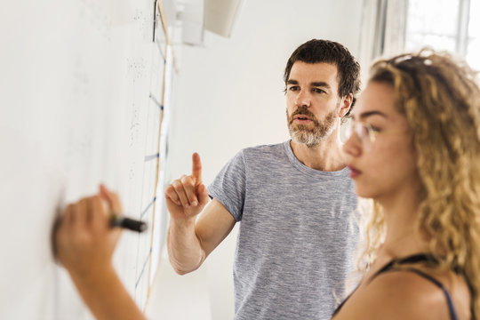 Student (14-15) writing on whiteboard, teacher looking