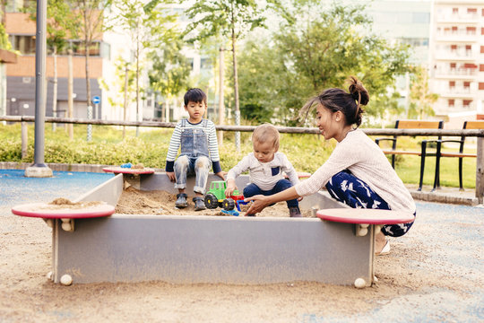 Mother playing with sons (2-3, 4-5) in sandbox