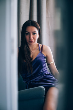 Sexy beautiful girl posing in a  room with violet dress, photographed in a paparazzi styl,spied style with foreground unfocused