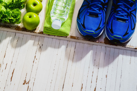 Fitness, healthy and active lifestyles Concept, dumbbells, sport shoes,  smartphone, bottle of water, apples and vegetable on wood background. copy space, top view