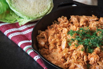 Delicious stewed cabbage in iron pan on dark rustic background, with the ingredients for this dish.