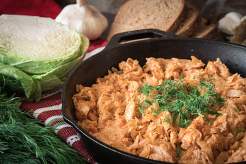 Delicious stewed cabbage in iron pan on dark rustic background, with the ingredients for this dish.
