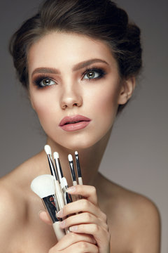 Fashion Woman Portrait. Girl Holding Bunch Of Makeup Brushes