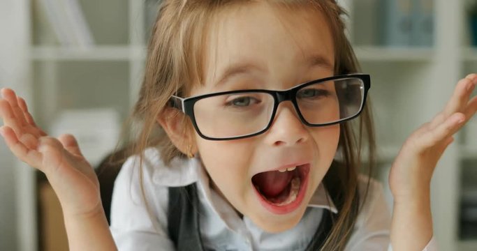 Very expressive young caucasian gir in glasses in formalwear crying by raising hands up. Close-up. Indoor.