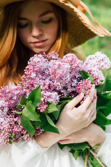 Naklejka premium Redhead girl with a bouquet of lilacs in a spring garden