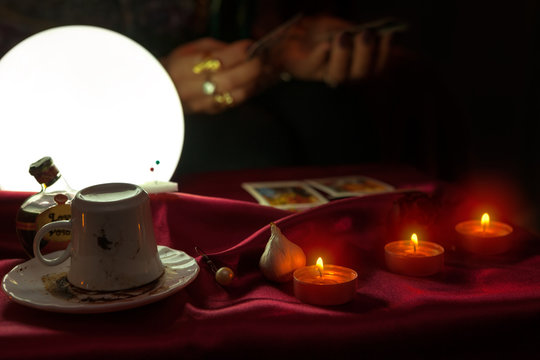 Coffee cup, candles and shiny crystal ball with tarot card in hand of fortune teller woman