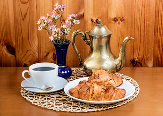 Cup of coffee, croissants and coffee pot on  table