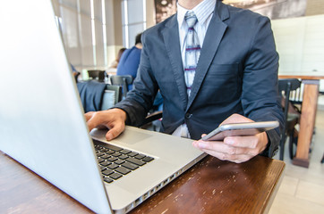 Business man mobile phone and laptop computer in coffee shop. City lifestyle business man hands working on typing on smartphone using 4G 5G wifi internet online service.