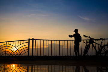 Fototapeta na wymiar Silhouette traveller taking photos of sunset. Travel by bicycle.