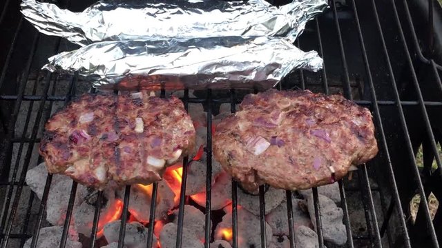 Video clip of burgers and two wrapped corn on the cob on a garden charcola bbq