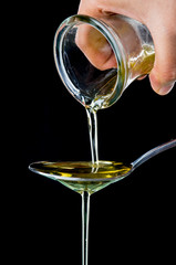 Olive oil pouring onto a spoon on black background
