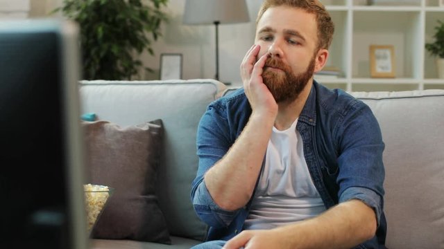 Attractive man with beard feeling borring and trying find some interesting film while sitting on sofa in the living room.