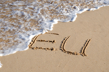 The word EU written in the sand and being washed away by the sea. Concept for failure of the European Union.