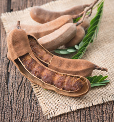 Sweet ripe tamarind pods with tamarind leaves on wood background