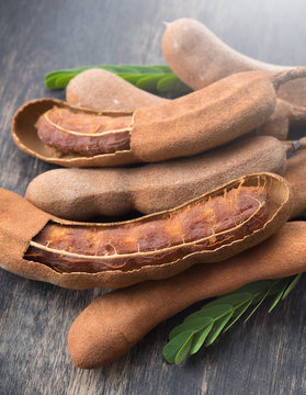 Sweet ripe tamarind pods with tamarind leaves on wood background