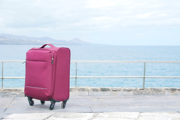 Travel suitcase outdoors, alone, with the sea in the background. Copyspace right.