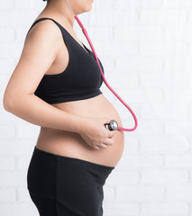 Pregnant woman listen for belly by stethoscope against white brick wall,Pregnancy concept
