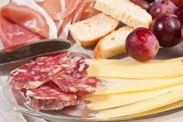 Close up ofGruyere cheese, grapes, salami, glass, red wine, cork, cheese knife, wood serving board, parings, tasty, savory healthy, lifestyle, wood bowl, brushchetta, artisan knife, italinan bread