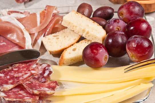 Close up ofGruyere cheese, grapes, salami, glass, red wine, cork, cheese knife, wood serving board, parings, tasty, savory healthy, lifestyle, wood bowl, brushchetta, artisan knife, italinan bread