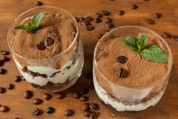 Two glasses with tiramisu, coffee beans and mint leaves. Dark background. Selective focus.