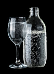 Bottle and glass of sparkling water over dark background