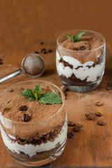 Two glasses with tiramisu, coffee beans and mint leaves. Dark background. Selective focus.