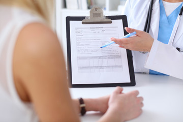 Fototapeta premium Close up of a doctor and patient hands while phisician pointing into medical history form at clipboard