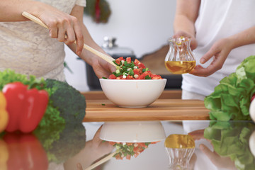 Close-up of four human hands are cooking in a kitchen. Friends having fun while preparing fresh salad. Vegetarian, healthy meal and friendship concept